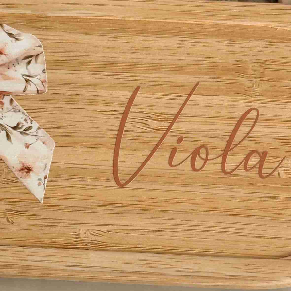 Personalisierte Edelstahl-Brotdose mit Bambusdeckel, floralem Schleifen-Motiv und dem Wunschnamen „Viola“.