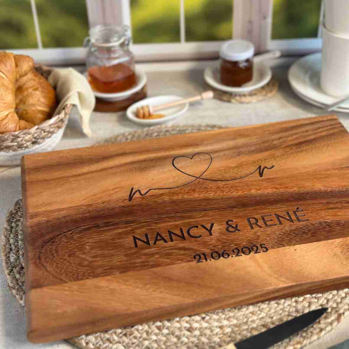 Personalisiertes Akazienholz-Schneidebrett mit Herzlinie, Gravur „Nancy & René“ und Datum 21.06.2025 in Frühstücksszene