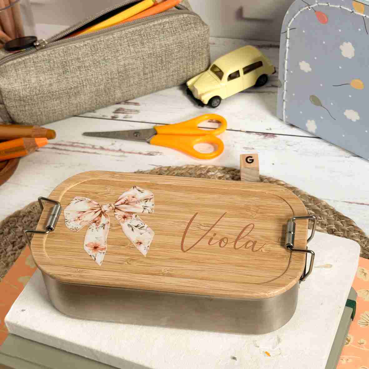 Personalisierte Edelstahl-Brotdose mit Bambusdeckel, floralem Schleifen-Motiv und dem Wunschnamen „Viola“.