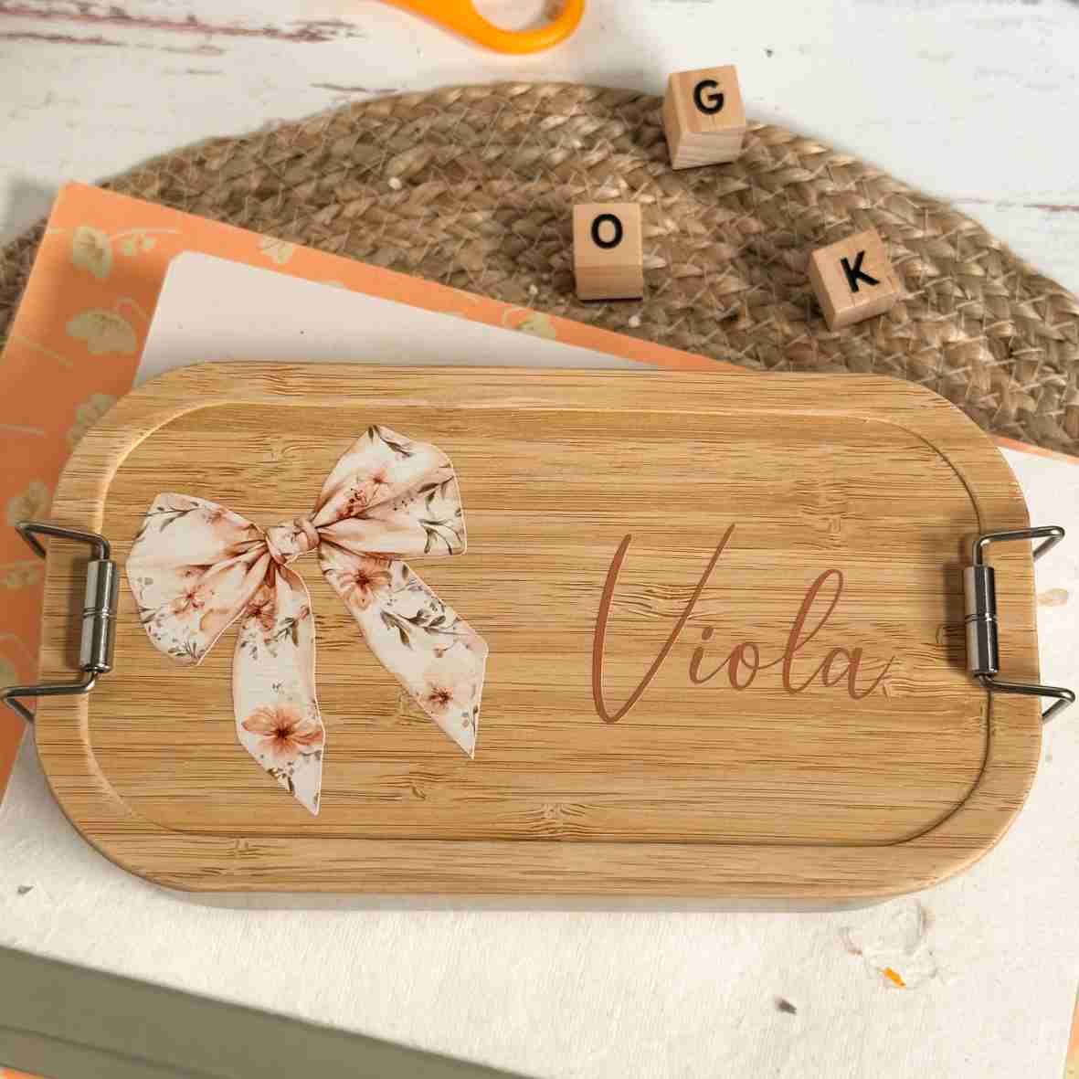 Personalisierte Edelstahl-Brotdose mit Bambusdeckel, floralem Schleifen-Motiv und dem Wunschnamen „Viola“.