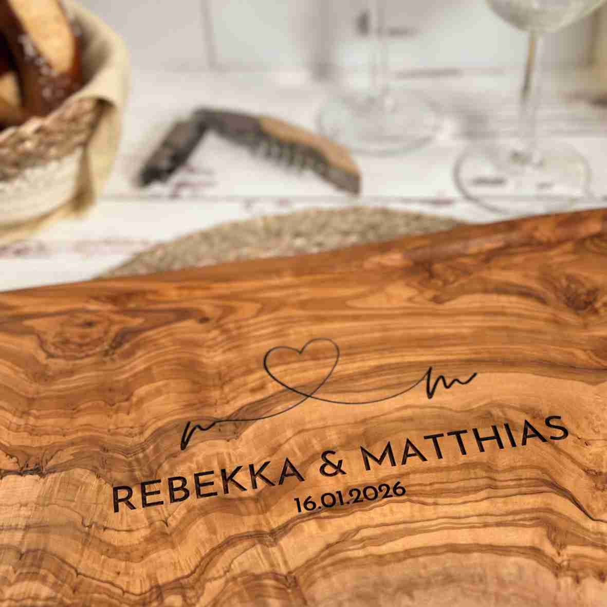 Personalisiertes Olivenholzbrett mit Herz-Gravur, Namen und Datum.