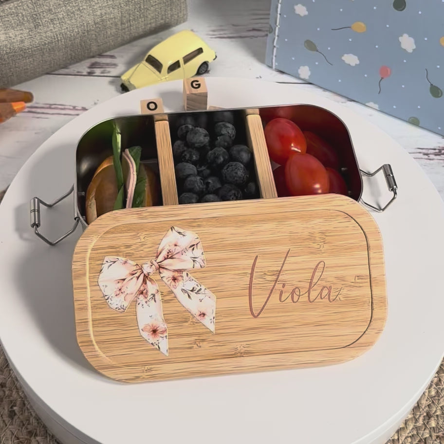 Personalisierte Edelstahl-Brotdose mit Bambusdeckel, floralem Schleifen-Motiv und dem Wunschnamen „Viola“.